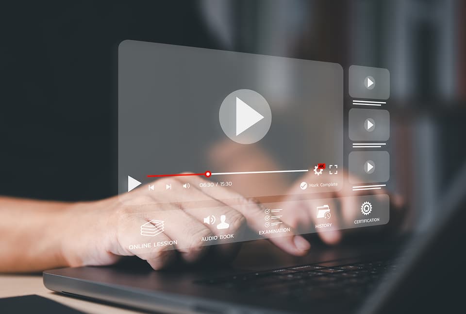 ノートパソコンを操作する手元に、再生ボタンや進行バーなど動画プレーヤーのUIが重なったデジタルイメージ